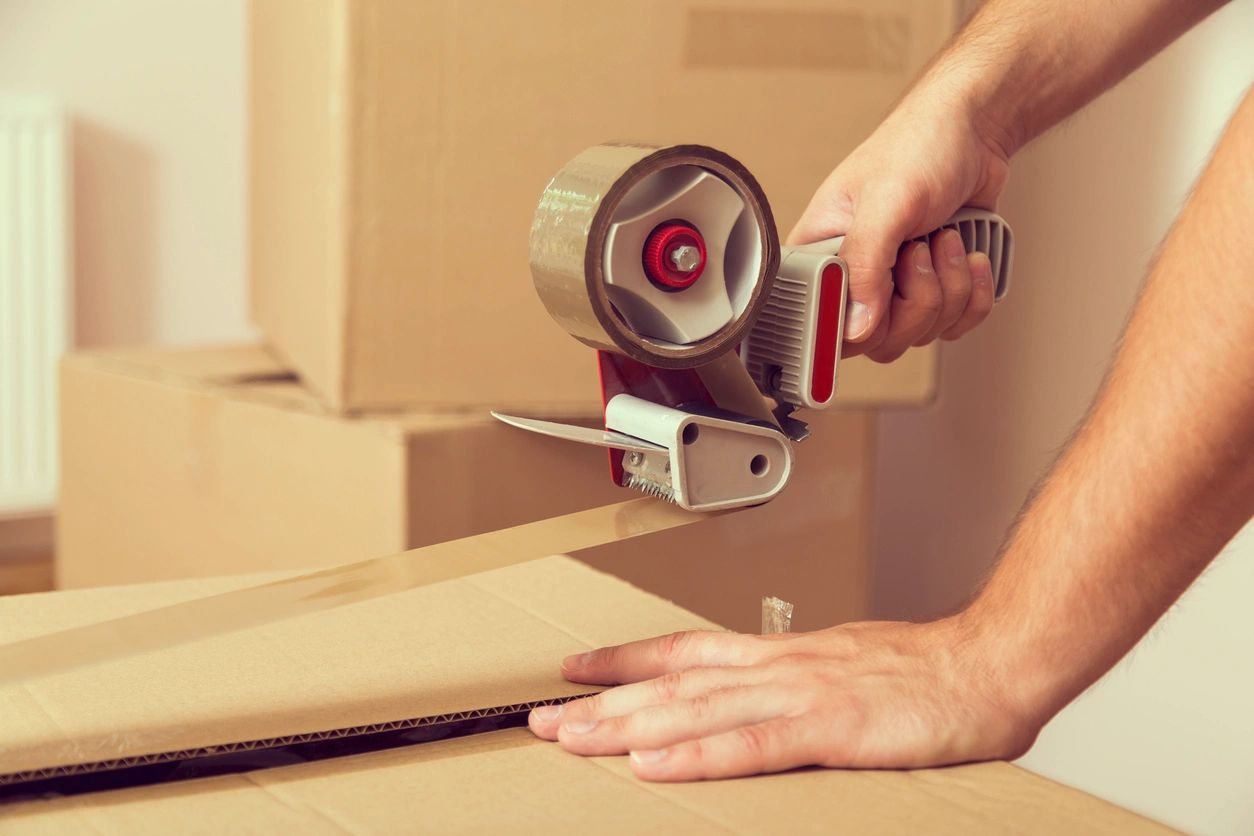 Close Up of a Guy's Hands Holding Packing Machine and Sealing Cardboard Boxes With Duct Tape